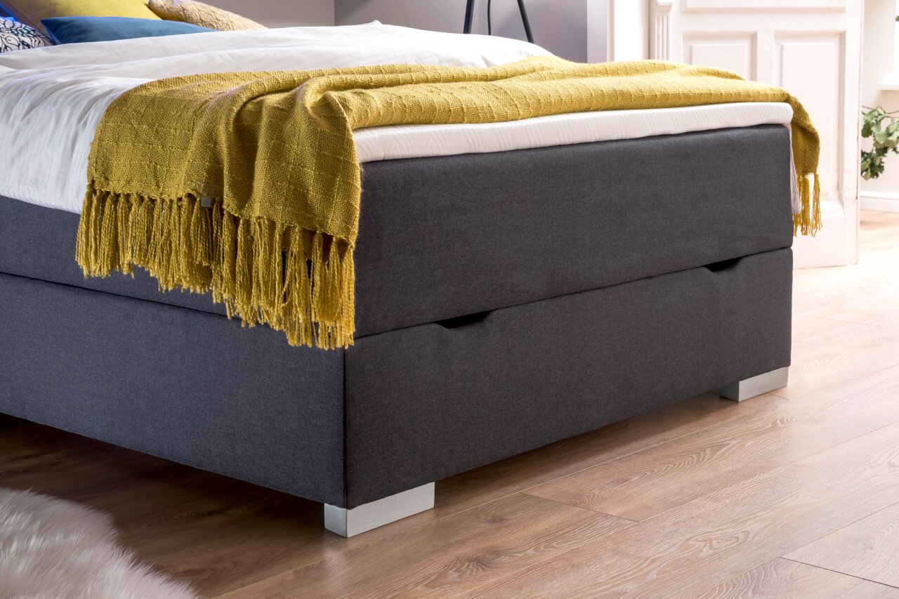 Boxbed met grijze stoffen bekleding en een geel dekbed, zijaanzicht