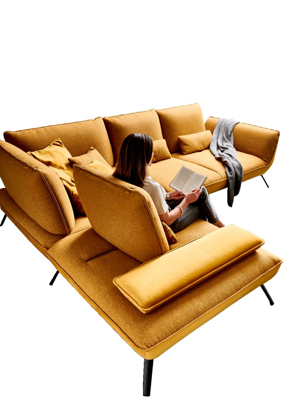 Eckgarnitur in senfgelber Farbe mit mehreren Kissen, auf der eine Person sitzt und ein Buch liest. Perspektive von oben.