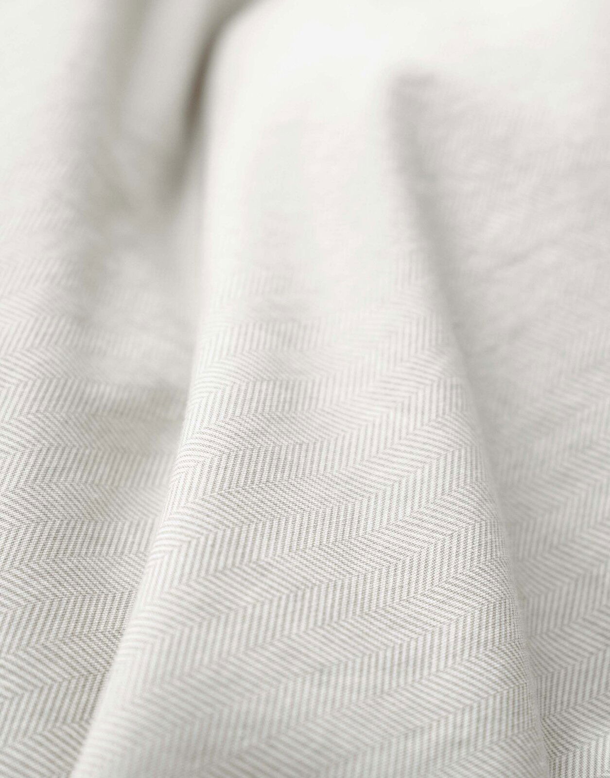 Nahaufnahme einer Bettwäsche mit dezentem Fischgrätenmuster in Beige.