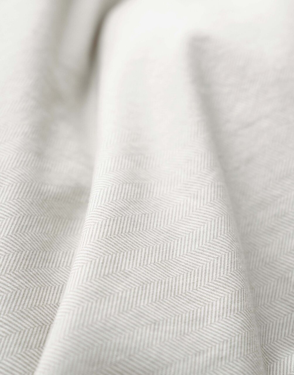 Nahaufnahme einer Bettwäsche mit dezentem Fischgrätenmuster in Beige.