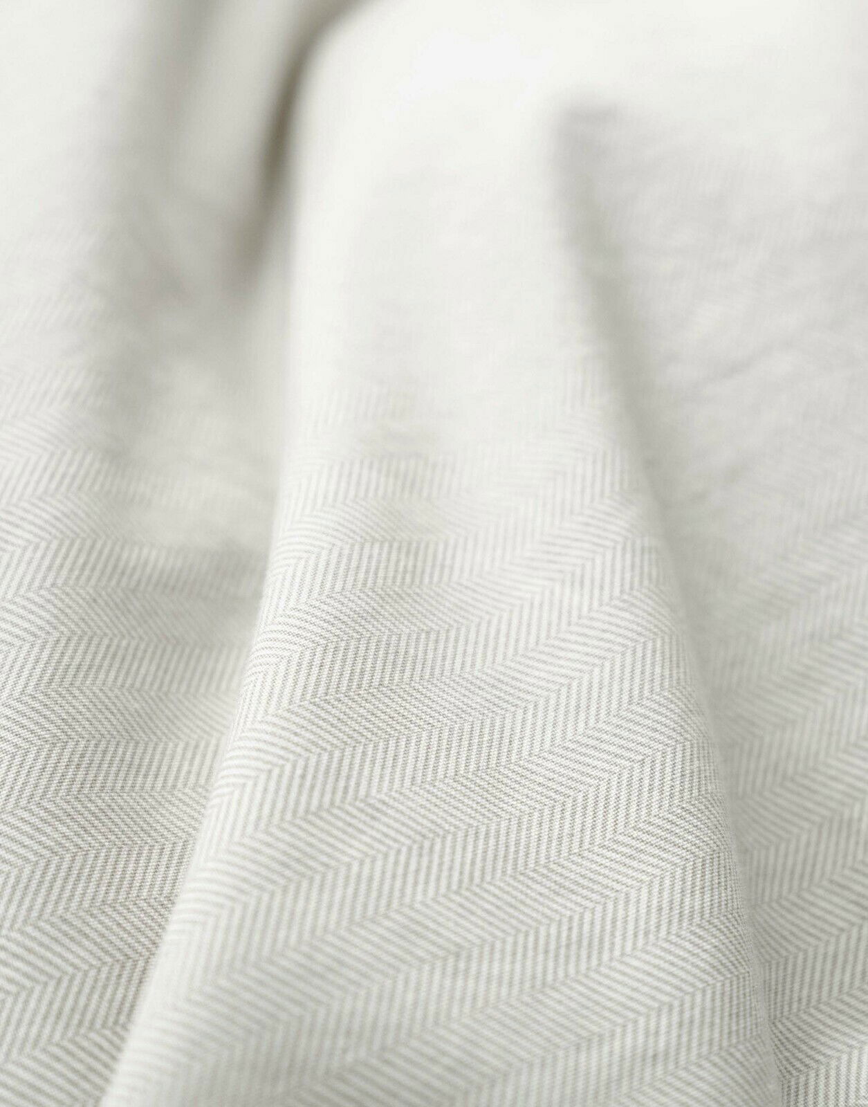 Nahaufnahme einer Bettwäsche mit dezentem Fischgrätenmuster in Beige.