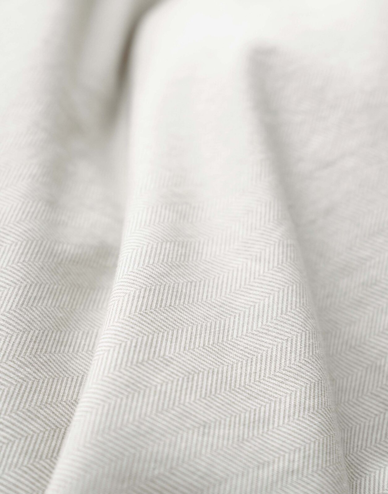 Close-up van beddengoed met een subtiel visgraatpatroon in beige.