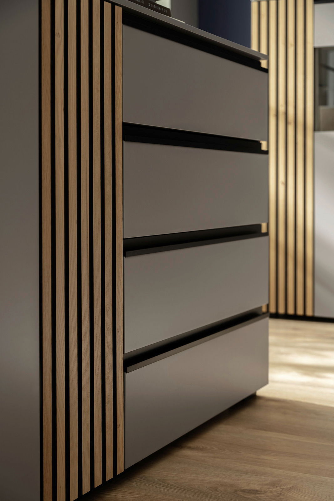 Nahaufnahme eines modernen Sideboards mit glatten, grauen Schubladen und vertikalen Holzelementen, seitliche Perspektive.