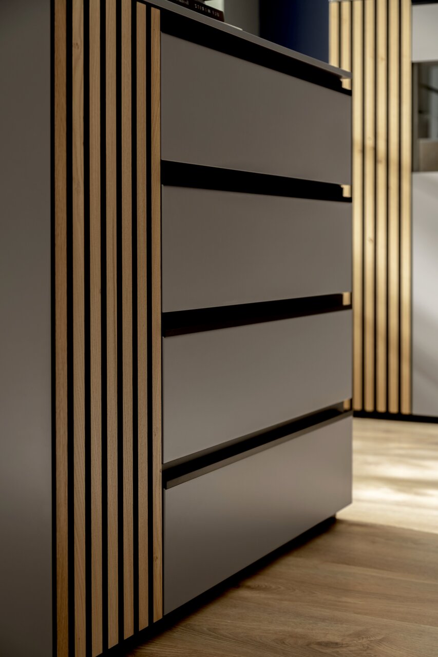 Nahaufnahme eines modernen Sideboards mit glatten, grauen Schubladen und vertikalen Holzelementen, seitliche Perspektive.