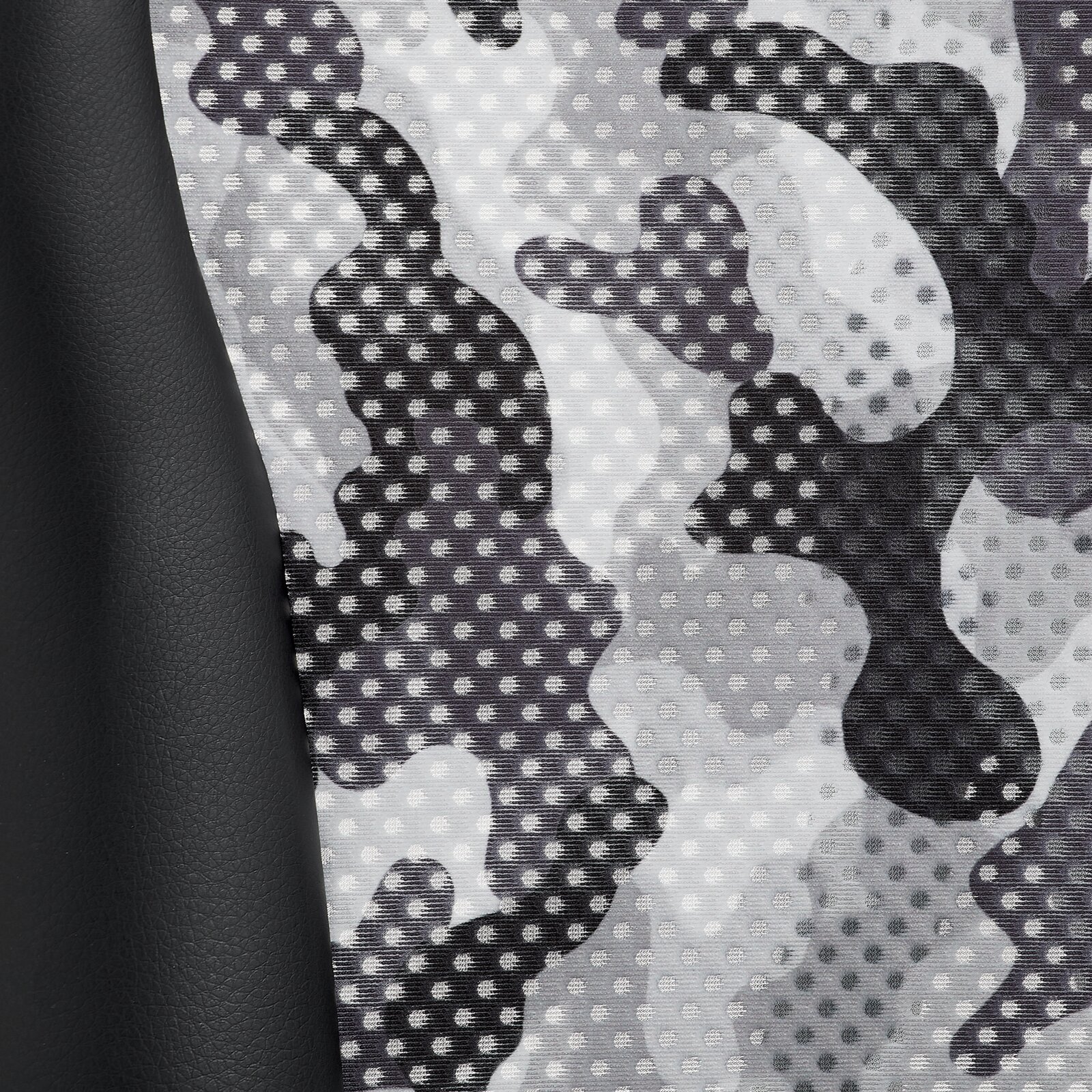 Close-up van het materiaal van een gamingstoel met een grijs camouflagepatroon en zwart kunstleer, gezien vanaf de zijkant