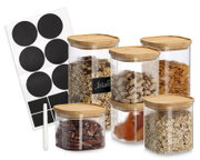 Set aus fünf transparenten Vorratsdosen mit geriffelter Oberfläche und Bambusdeckeln, gefüllt mit Müsli, Nüssen, Cornflakes, Haferflocken und Trockenfrüchten; daneben schwarze Etiketten-Aufkleber und Kreidestift, Produktansicht schräg von vorn leicht erhö