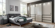 Modernes Polsterbett in einem stilvollen Schlafzimmer, seitliche Perspektive mit grauem Kopfteil und passendem Nachttisch.