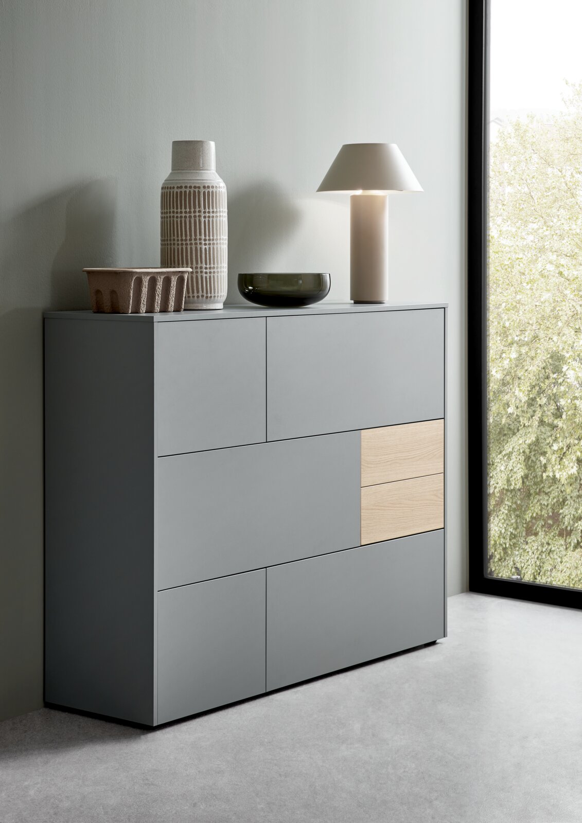 Modernes Highboard in Grau mit Holzakzent, seitliche Perspektive, dekoriert mit Vasen und Lampe.
