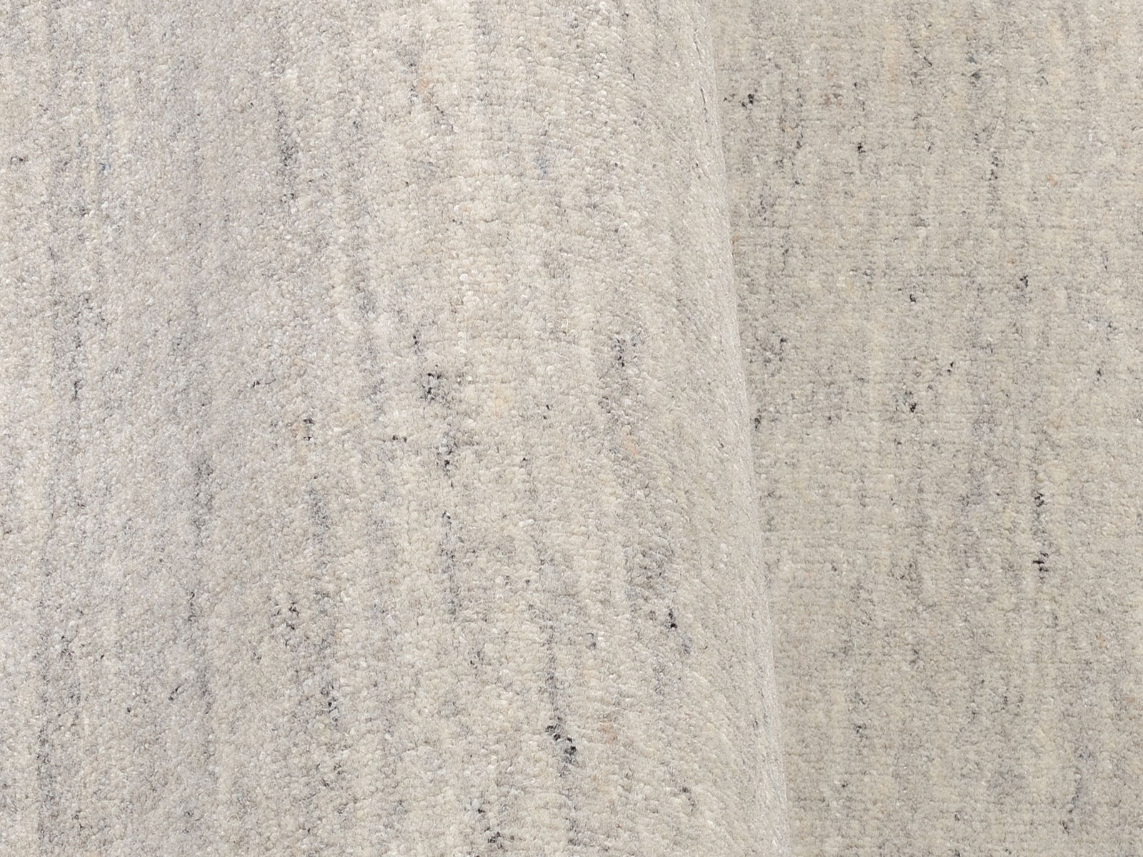 Nahaufnahme eines hellen Wollteppichs mit dezenter Musterung, seitliche Perspektive