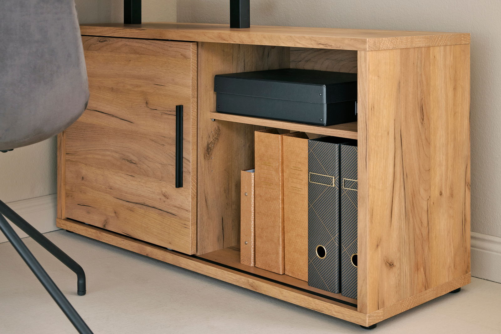 Nahaufnahme eines Eck-Schreibtisch-Kombinationselements aus Holz mit einem Schrank und Regalfächern, gefüllt mit Ordnern und einer Box, von der Seite betrachtet.