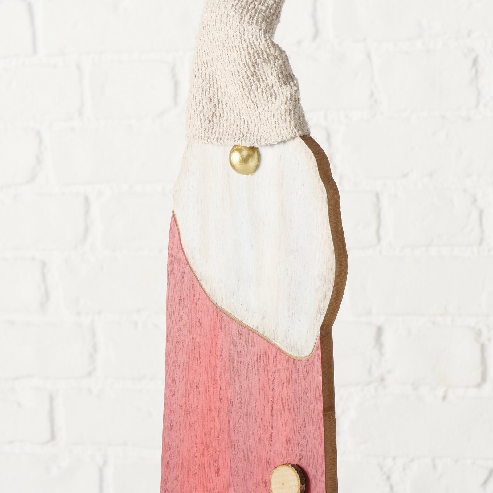 Nahaufnahme einer dekorativen Figur mit rotem Körper, weißem Bart und gestrickter Mütze, seitliche Perspektive.