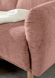 Nahaufnahme einer rosafarbenen Sofaecke mit weicher Textur und Holzbeinen, von der Seite betrachtet.