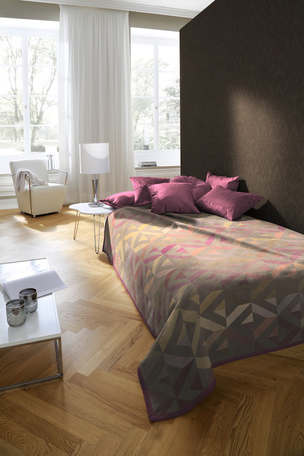 Bett mit geometrisch gemusterter Decke in einem modernen Schlafzimmer, seitliche Perspektive