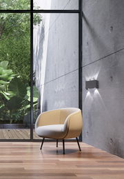 Moderne Wandleuchte Nair an einer Betonwand, seitliche Perspektive mit Blick auf einen Sessel und einen Garten im Hintergrund.