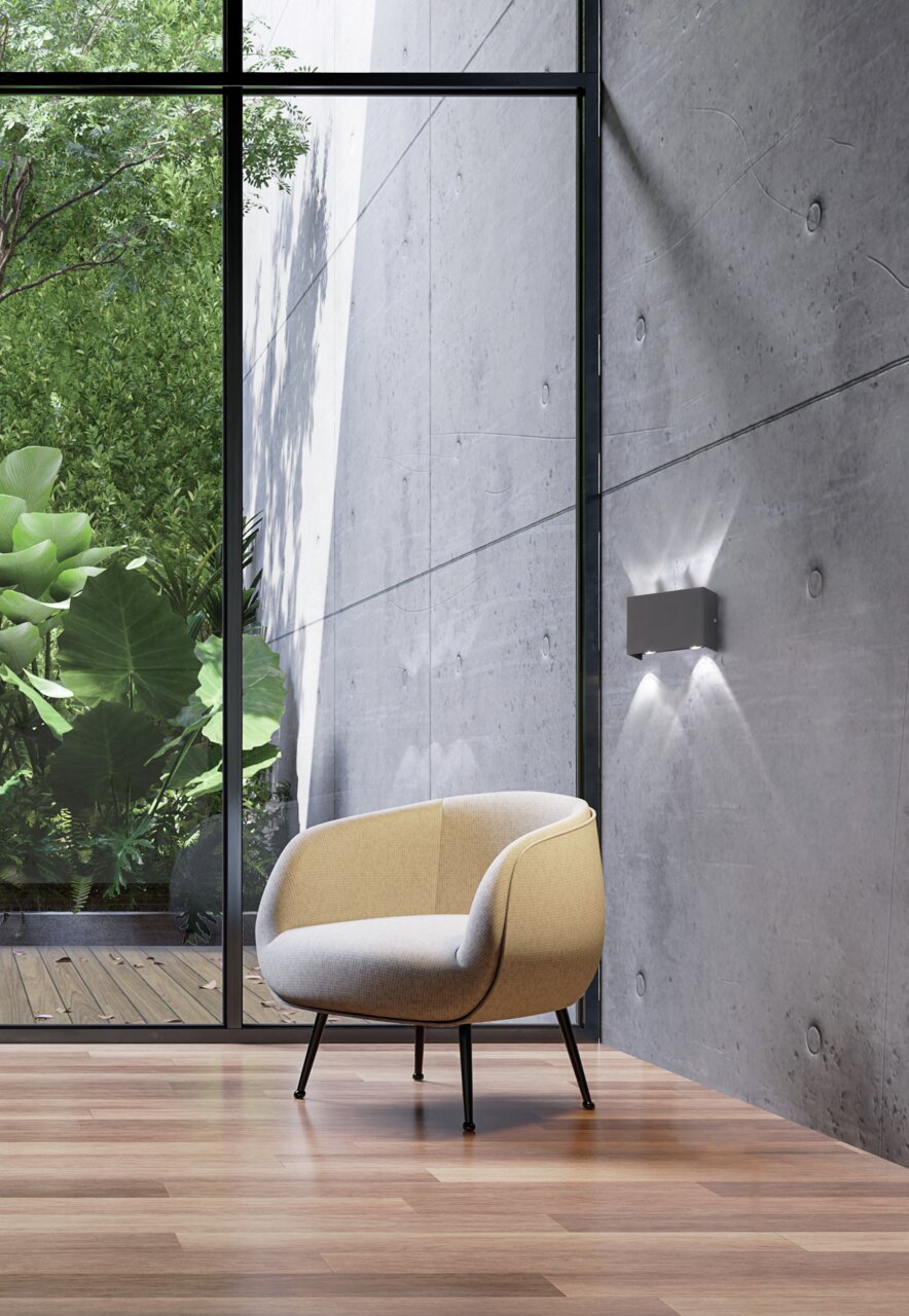 Moderne Wandleuchte Nair an einer Betonwand, seitliche Perspektive mit Blick auf einen Sessel und einen Garten im Hintergrund.