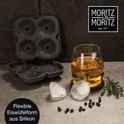 Perspektive von oben: Eine geöffnete, flexible Eiswürfelform aus Silikon mit vier runden Formen, daneben ein Glas mit Getränk und runde Eiswürfel auf einem Tisch.