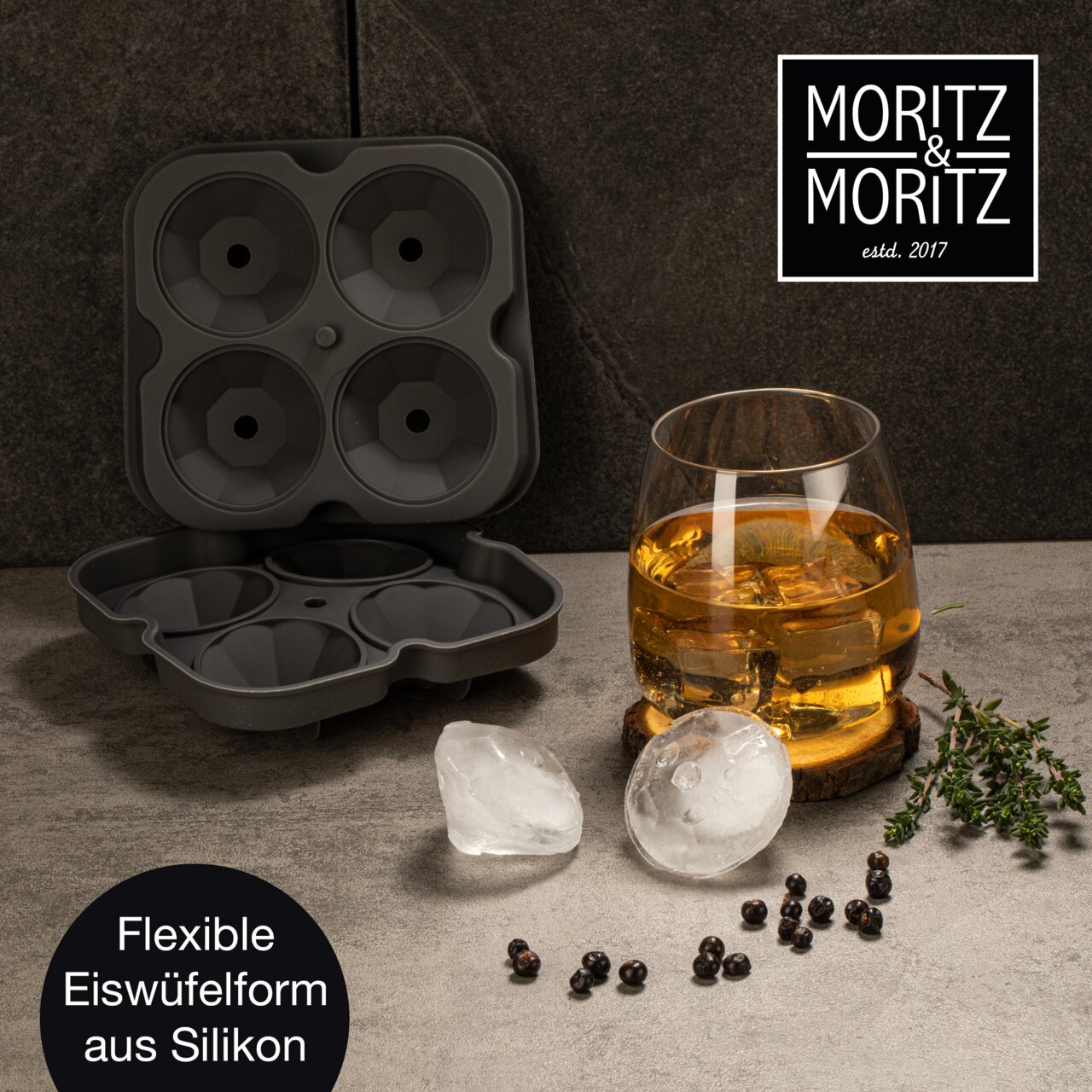 Perspektive von oben: Eine geöffnete, flexible Eiswürfelform aus Silikon mit vier runden Formen, daneben ein Glas mit Getränk und runde Eiswürfel auf einem Tisch.