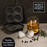 Perspektive von oben: Eine geöffnete, flexible Eiswürfelform aus Silikon mit vier runden Formen, daneben ein Glas mit Getränk und runde Eiswürfel auf einem Tisch.