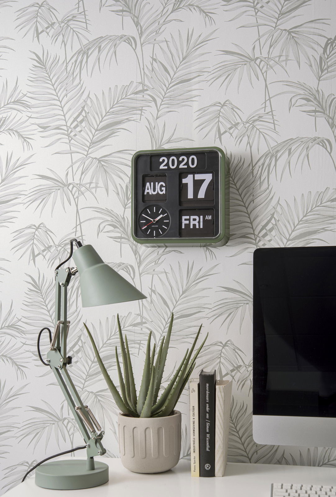 Wanduhr Mini in einem modernen Raum mit Pflanzenmotiv-Tapete, Schreibtischlampe und Computer, seitliche Perspektive