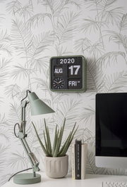 Mini-wandklok in een moderne kamer met behang met plantenmotief, bureaulamp en computer, zijaanzicht