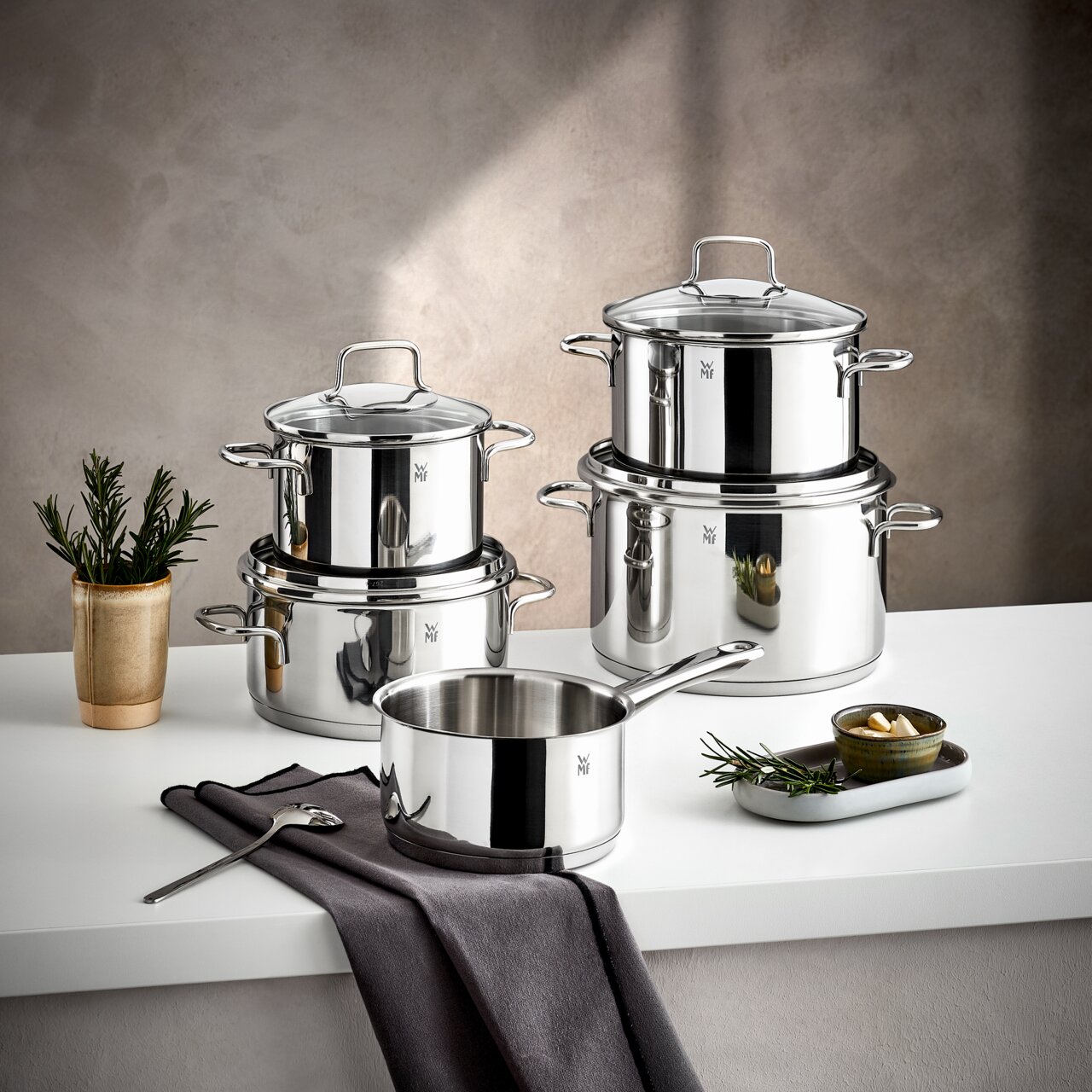 Topfset Astoria 5-tlg. aus Edelstahl, bestehend aus mehreren Töpfen und einem Stieltopf, auf einem Tisch arrangiert, seitliche Perspektive.