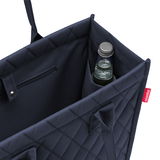 Nahaufnahme einer dunkelblauen Einkaufstasche mit Rautenmuster, die eine Flasche in einem Seitenfach zeigt.