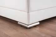 Nahaufnahme der Ecke eines weißen Polsterbetts mit metallischen Füßen auf einem Holzboden, Perspektive von unten.