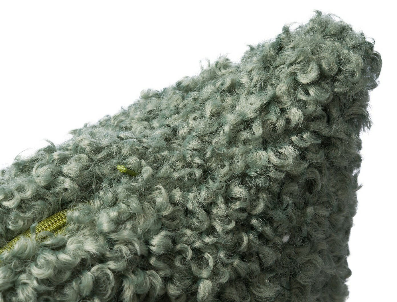 Nahaufnahme einer grünen, flauschigen Kissenhülle mit lockiger Textur, perspektivisch von der Seite aufgenommen.