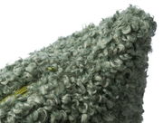 Nahaufnahme einer grünen, flauschigen Kissenhülle mit lockiger Textur, perspektivisch von der Seite aufgenommen.
