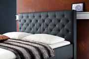 Seitliche Ansicht eines eleganten Polsterbetts mit gesteppter Kopfstütze in dunklem Leder, dekoriert mit weißen Kissen und einer gestreiften Decke.