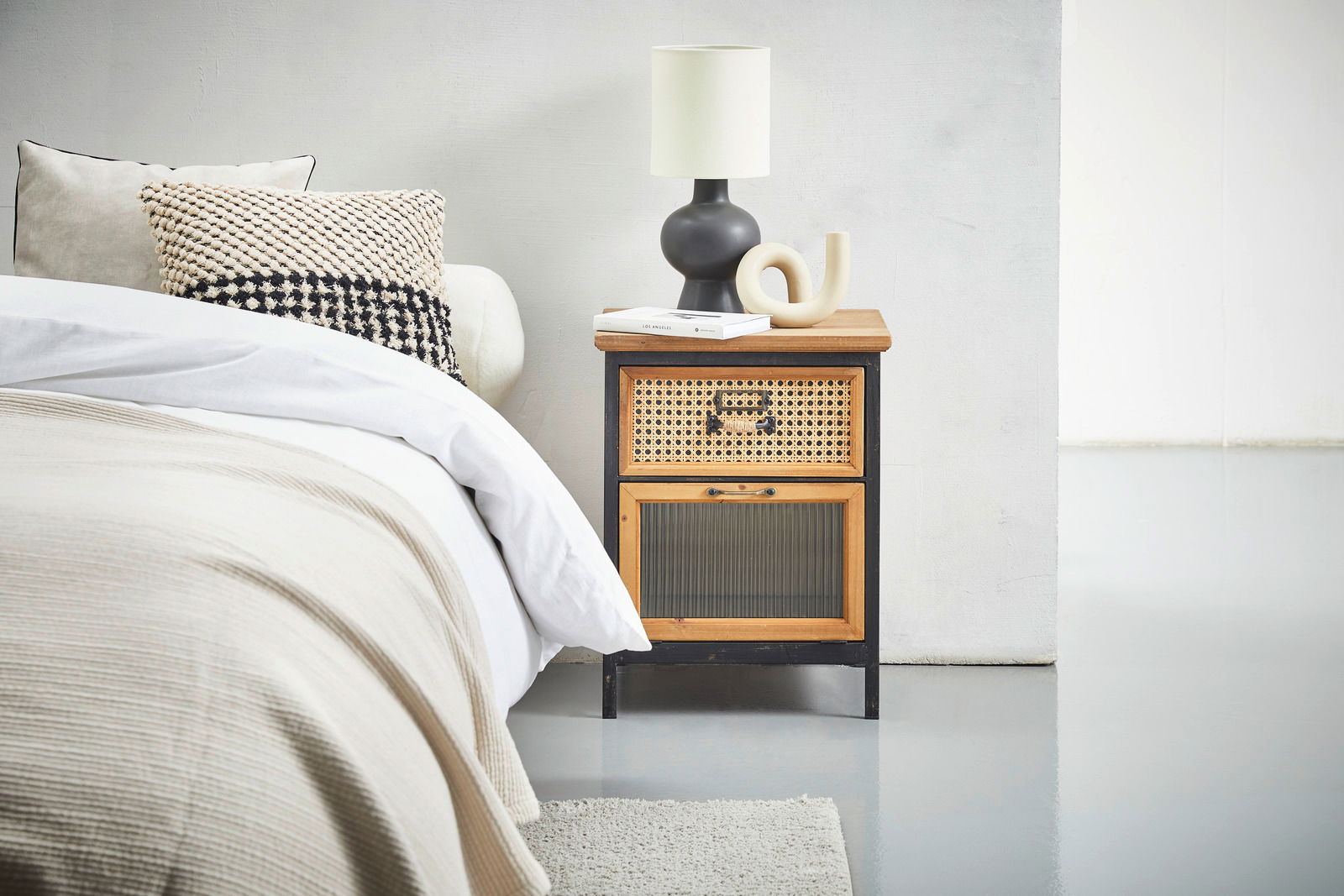 Nachtkommode aus Holz mit Rattandetails, seitliche Perspektive, dekoriert mit Lampe und Büchern.