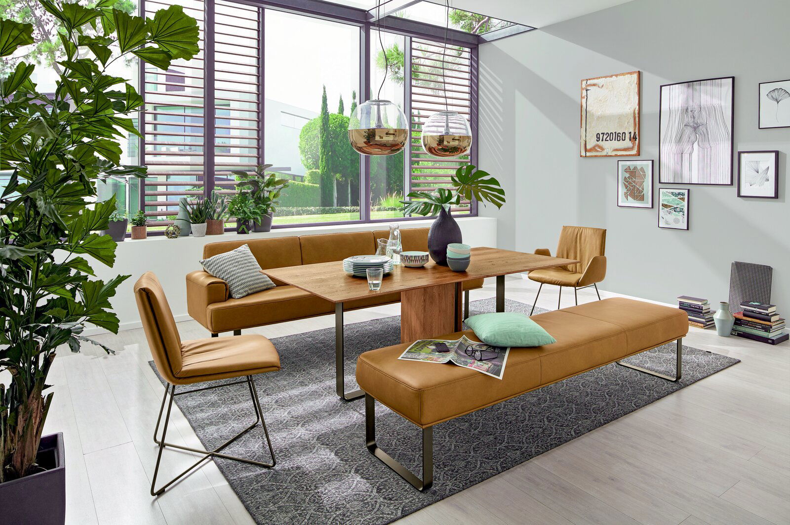 Moderner Esstisch aus Holz mit braunen Lederstühlen und -bänken in einem hellen, stilvoll eingerichteten Raum mit großen Fenstern und Pflanzen, seitliche Perspektive.
