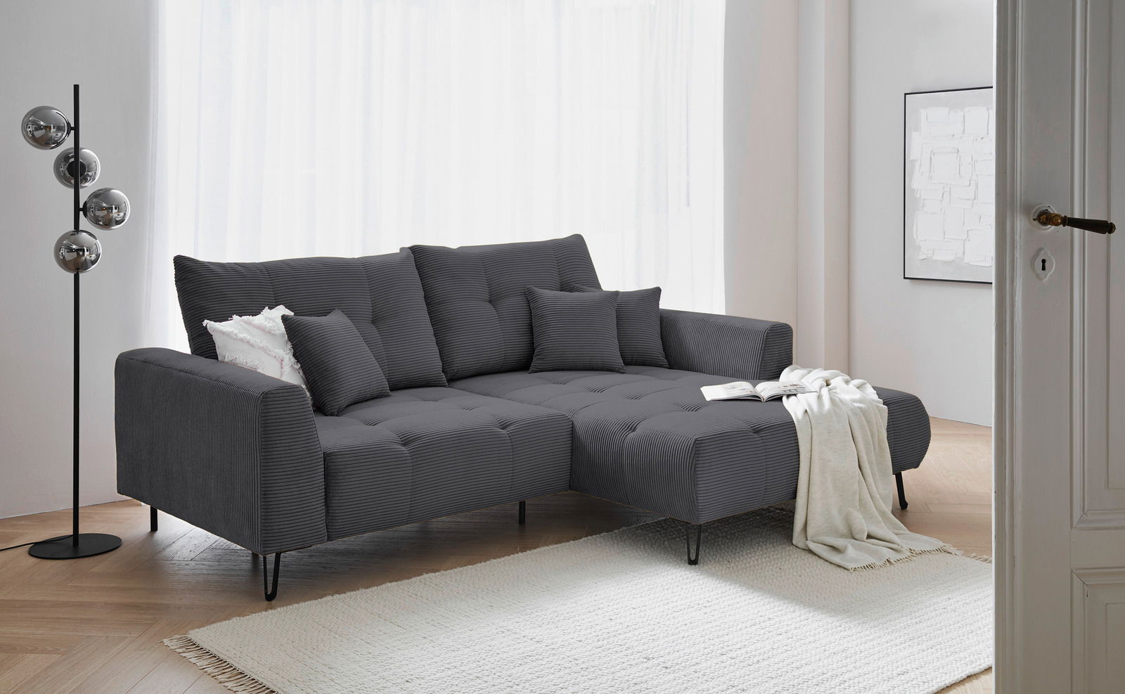 Z2 Hoekbank SWING Graues Ecksofa mit Ottomane rechts, dekoriert mit Kissen und Decke, in einem modernen Wohnzimmer mit hellem Holzboden und Stehlampe, seitliche Perspektive.