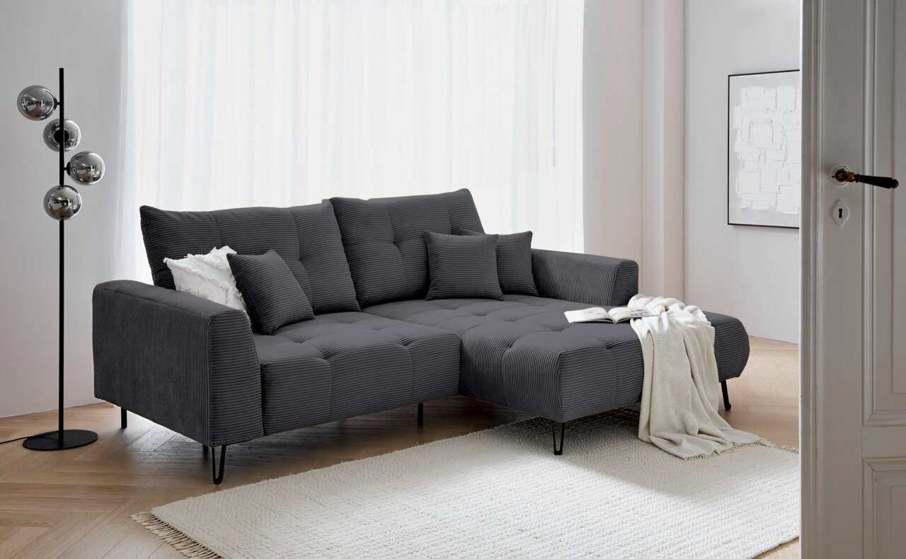 Z2 Ecksofa SWING Graues Ecksofa mit Ottomane rechts, dekoriert mit Kissen und Decke, in einem modernen Wohnzimmer mit hellem Holzboden und Stehlampe, seitliche Perspektive.