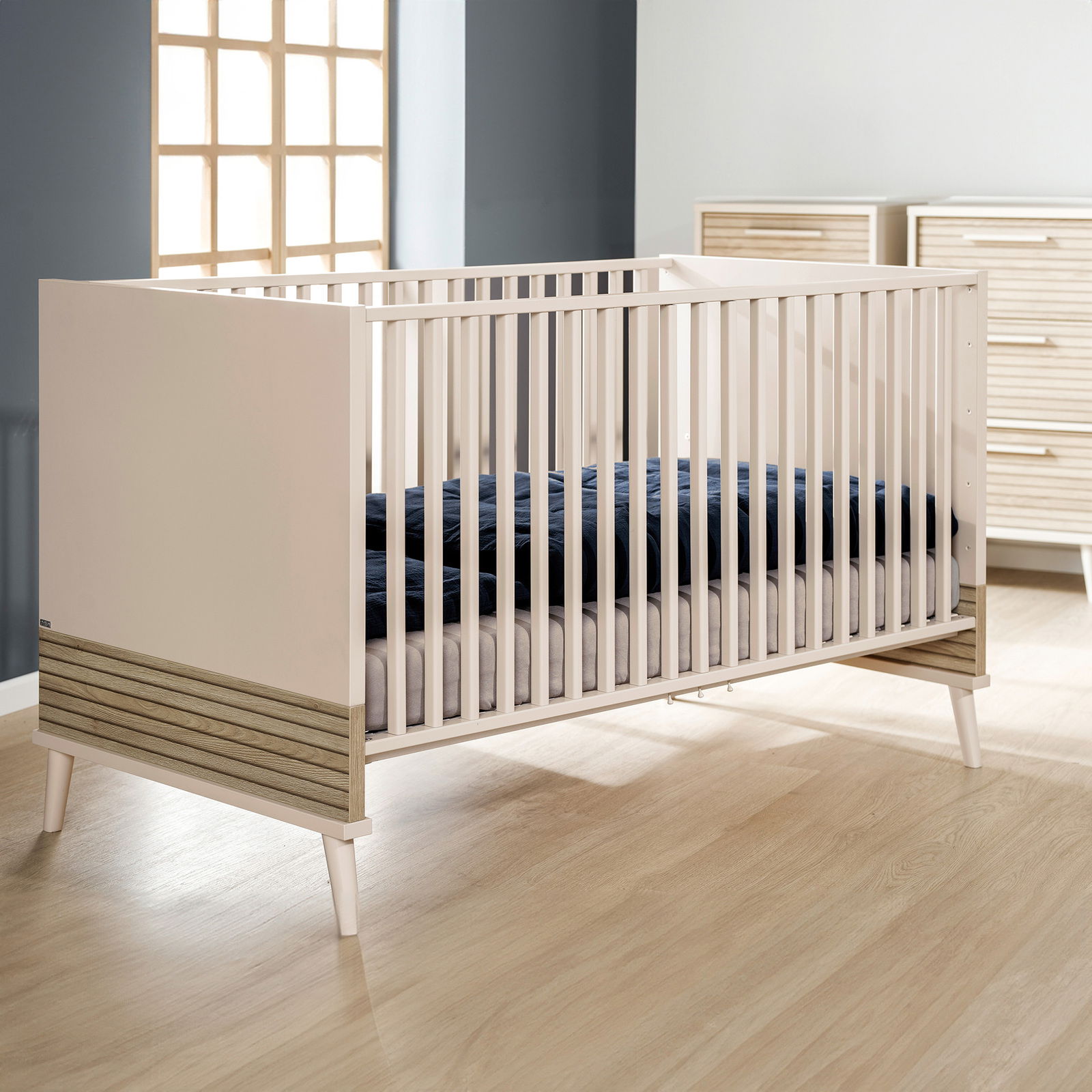 Modernes Babybett aus Holz mit weißen Gitterstäben, seitliche Perspektive, in einem stilvollen Kinderzimmer.