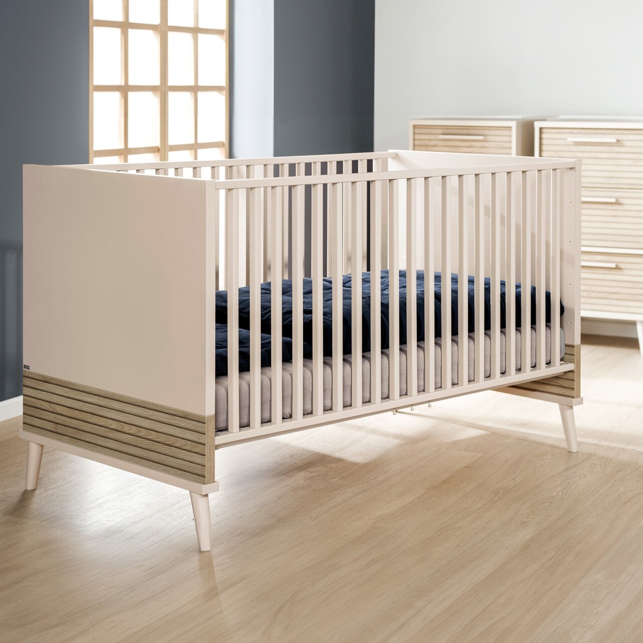 Modern houten babybedje met witte spijlen, gezien vanaf de zijkant, in een stijlvolle kinderkamer.