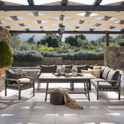 Lounge-Set auf einer Terrasse mit Blick auf einen Garten, bestehend aus einem Tisch und mehreren Sesseln, umgeben von Natursteinmauern und Pergola.