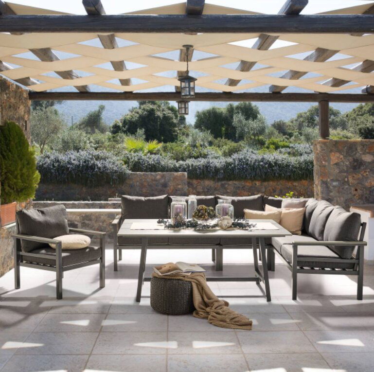 Lounge-Set auf einer Terrasse mit Blick auf einen Garten, bestehend aus einem Tisch und mehreren Sesseln, umgeben von Natursteinmauern und Pergola.