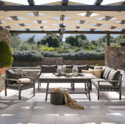 Lounge-Set auf einer Terrasse mit Blick auf einen Garten, bestehend aus einem Tisch und mehreren Sesseln, umgeben von Natursteinmauern und Pergola.