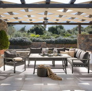 Lounge-Set auf einer Terrasse mit Blick auf einen Garten, bestehend aus einem Tisch und mehreren Sesseln, umgeben von Natursteinmauern und Pergola.