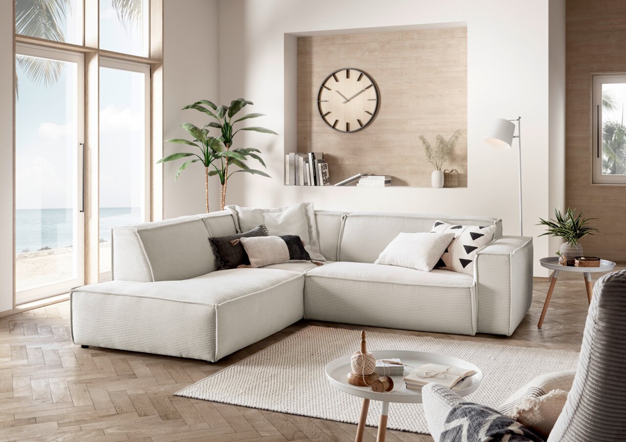 Eckkombination in einem modernen Wohnzimmer mit Blick auf das Meer durch große Fenster, helle Polsterung und dekorative Kissen.
