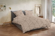 Beige Bettwäsche mit geometrischem Linienmuster in Braun auf einem grauen Polsterbett, frontal in leichter Schrägansicht von vorn fotografiert, im hellen Schlafzimmer-Setting mit goldener Stehlampe und Kleiderständer.