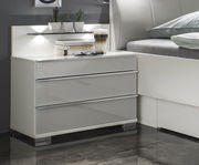 Moderne Nachtkonsole mit drei Schubladen in Hochglanzoptik, seitliche Perspektive, dekoriert mit Büchern, Brille und Kaktuspflanzen.