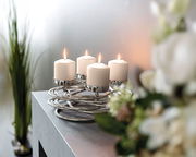 Moderner silberner Kerzenhalter mit vier brennenden weißen Kerzen, auf einem Tisch von schräg oben fotografiert.