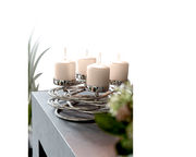 Moderner silberner Kerzenhalter mit vier brennenden weißen Kerzen, auf einem Tisch von schräg oben fotografiert.