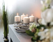 Moderner silberner Kerzenhalter mit vier brennenden weißen Kerzen, auf einem Tisch von schräg oben fotografiert.