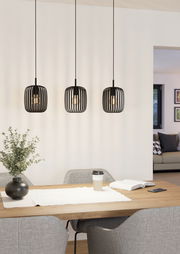 Drei moderne, schwarze Pendelleuchten Romazzina hängen über einem Esstisch in einem stilvoll eingerichteten Raum. Perspektive von vorne.
