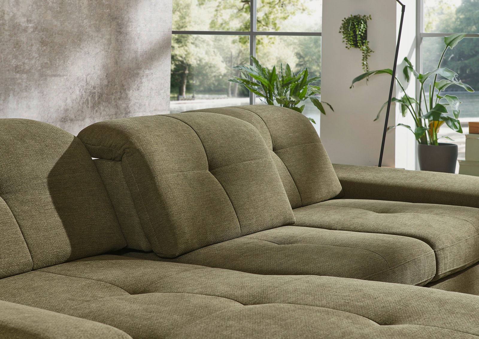 Grüne Longchairkombination in einem modernen Wohnzimmer mit großen Fenstern und Pflanzen, seitliche Perspektive