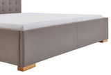 Polsterbett in seitlicher Perspektive mit grauem Stoffbezug und Holzfüßen.