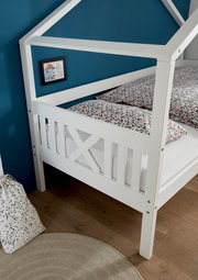 Weißes Hausbett mit Gitterdesign, seitliche Perspektive, vor einer blauen Wand mit gemusterten Bettbezügen.